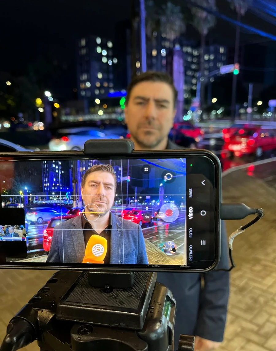 Fernando Zanuzo em entrada ao vivo à noite, com a cidade ao fundo