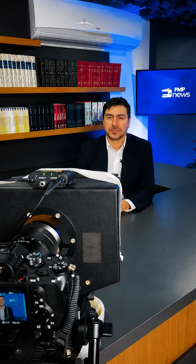 Fernando Zanuzo na bancada do FMP News, com a câmera de gravação em primeiro plano